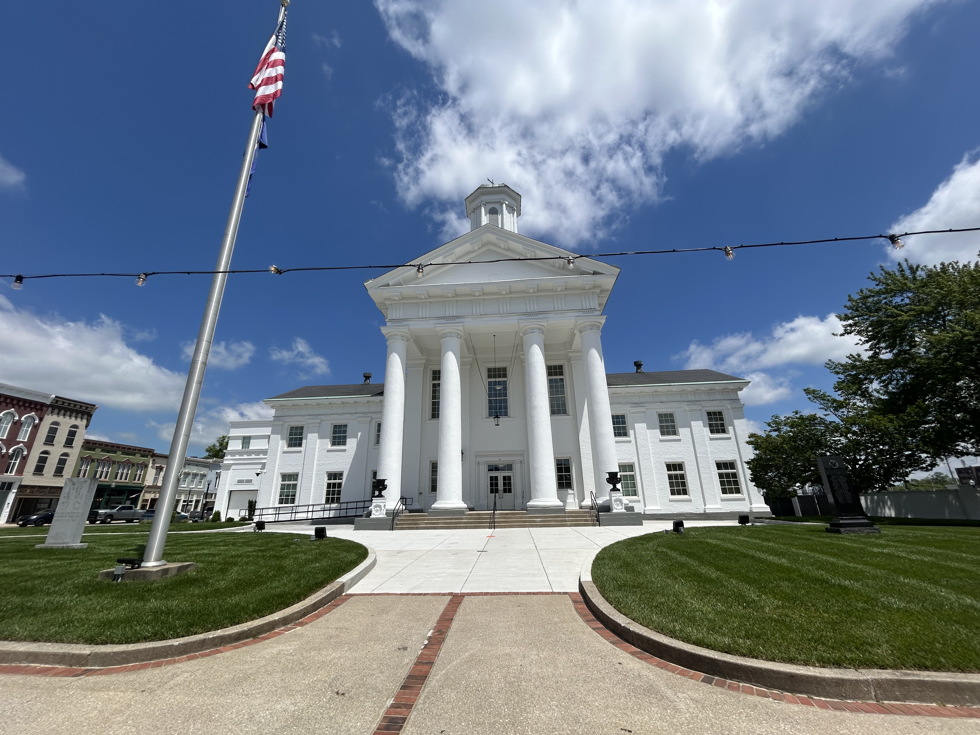 A large white pillar courthouse with green grass and U.S. flag flown.