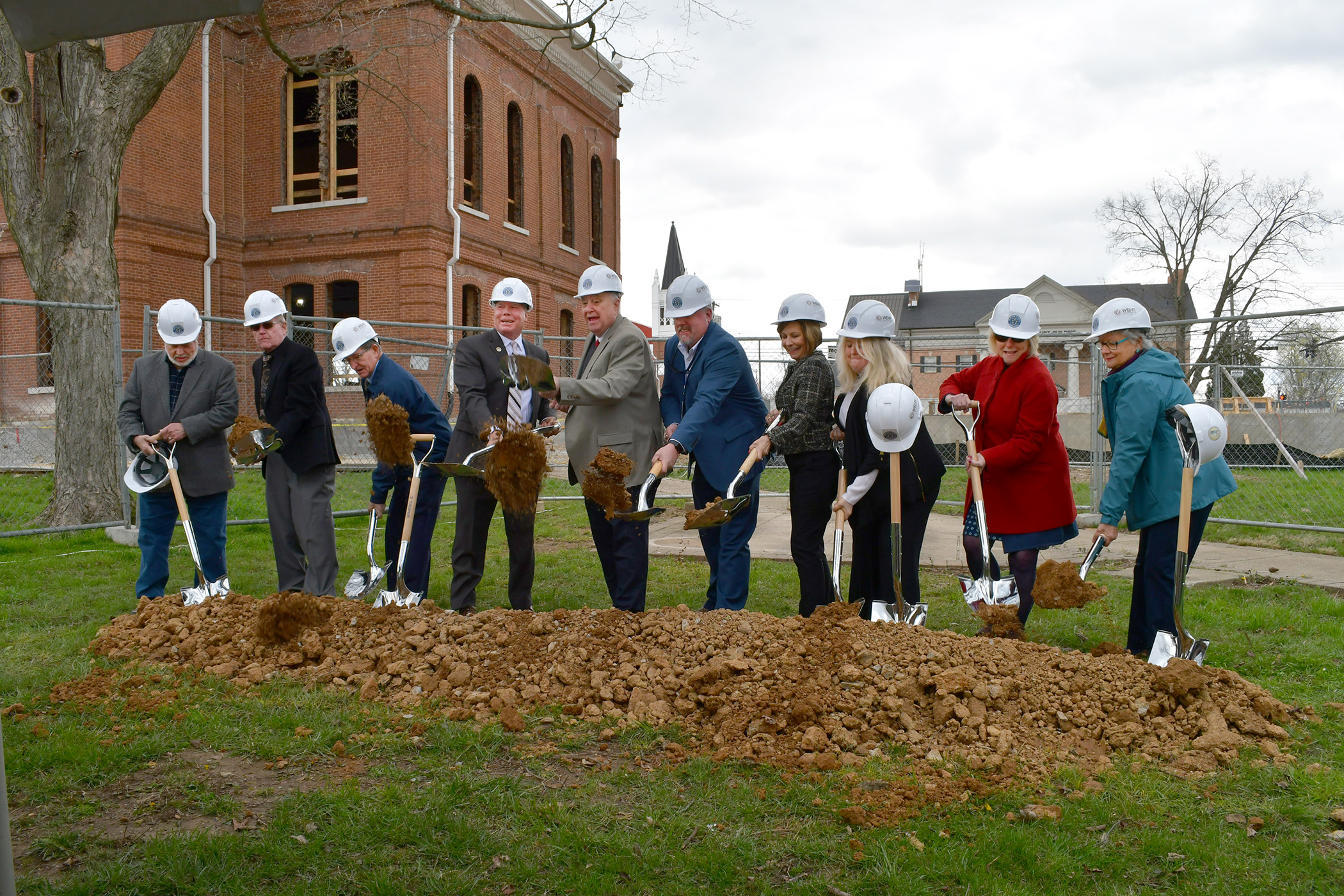 A group of individuals shoveling dirt with hard hats.