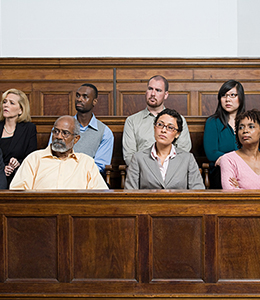 A jury of multiple people seated in a courtroom, attentively listening. The individuals are arranged in courtroom rows.